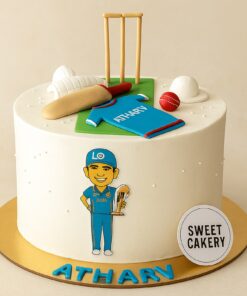 Cricket theme birthday cake from Sweet Cakery with cream finish, decorated with fondant bat, ball, stumps, gloves, jersey and player design.