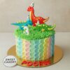 One-tier dinosaur theme birthday cake with colourful dinos, grassy green top, and pastel side design. Sweet Cakery branding on sticker in front.