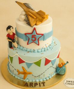 Two-tier fighter jet theme birthday cake with fondant jet, star badge, bunting, and boy figurine, created by Sweet Cakery in Bangalore