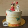Girl with puppy theme birthday cake from Sweet Cakery, featuring a doll topper in red dress, cute puppy figurine, balloons, butterflies, and pearl accents on cream finish.