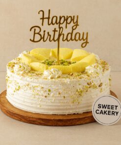 Rasmalai flavour birthday cake by Sweet Cakery, topped with rasmalai pieces, pistachios, white cream frosting, and gold Happy Birthday topper.