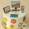 Social media lover cake from Sweet Cakery with cream icing, decorated with app icons, computer monitor, headphones and stationery topper.