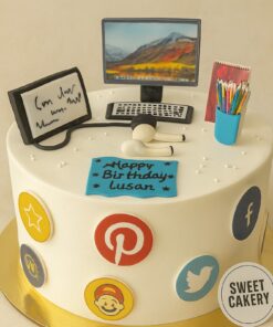 Social media lover cake from Sweet Cakery with cream icing, decorated with app icons, computer monitor, headphones and stationery topper.