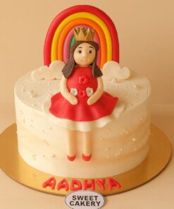 Rainbow princess theme birthday cake for girls with red fondant gown, crown topper, colourful rainbow, and Sweet Cakery branding on the board.