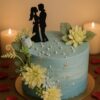 Blue cake with floral decorations, pearl beads, silver leaf, and romantic couple silhouette topper