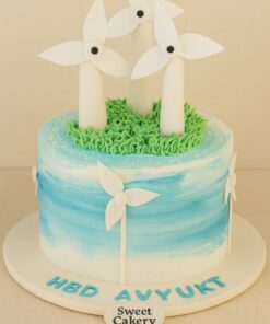 Windmill theme birthday cake with edible fondant turbines, blue gradient buttercream, hand-piped grass, and Sweet Cakery sticker in Bangalore.