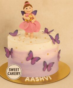 A round pastel cream cake with a fairy doll topper, purple butterflies, and gold accents, made by Sweet Cakery in Bangalore for a butterfly-themed birthday
