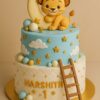 Lion Theme First Birthday Cake by Sweet Cakery in Bangalore. Two-tier cake with a cartoon cub on a crescent moon, quilted base, stars, clouds, and decorative spheres. Perfect for first birthdays, six month birthdays, and young kids’ birthday parties.
