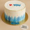 Sweet Cakery’s romantic “Love You” cake with smooth white buttercream, red heart topper, blue fondant lettering, gold accents.