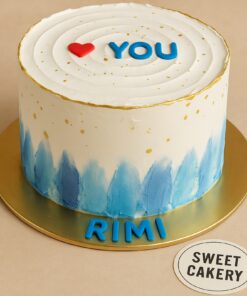 Sweet Cakery’s romantic “Love You” cake with smooth white buttercream, red heart topper, blue fondant lettering, gold accents.